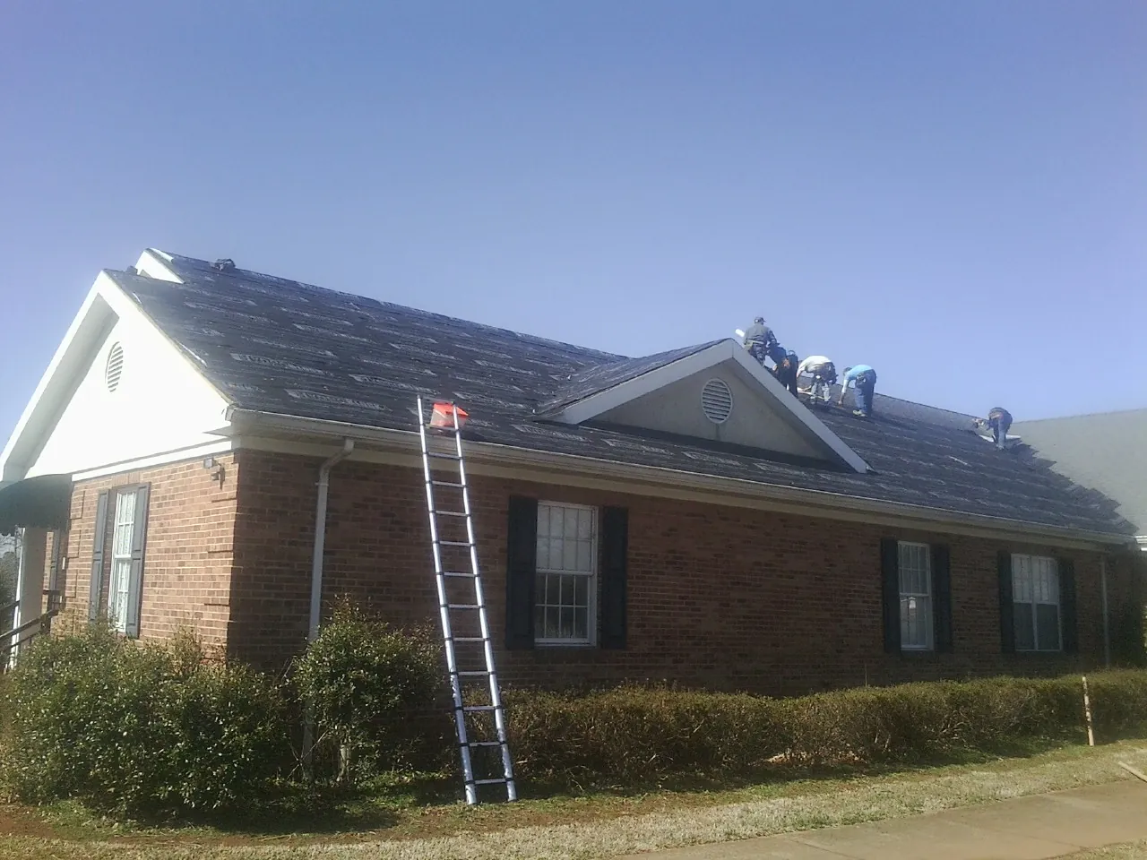 Crew tearing shingles off a brick ranch roof with a ladder set — Metal Roof Repair work by our crew in Cleveland